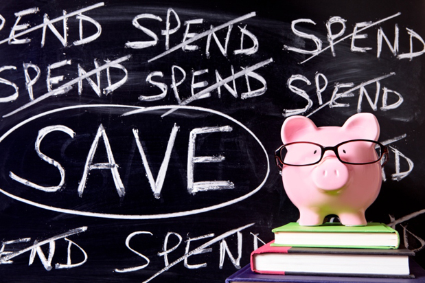 Pink piggy bank with glasses standing on books next to a blackboard with untidy spending and saving message.